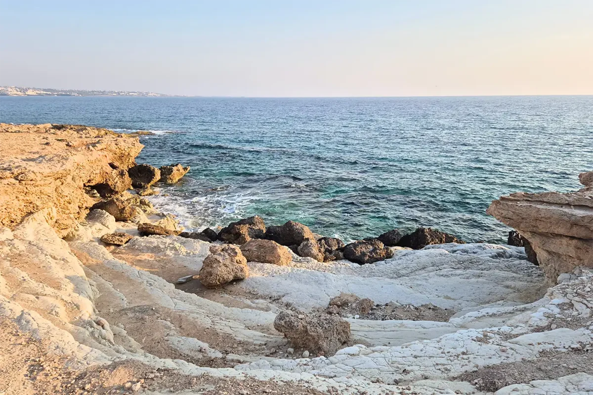 Küstenlandschaft mit Felsen und ruhigem türkisblauem Meer bei Sonnenuntergang.