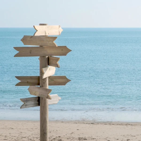 Holzwegweiser am Strand vor dem Meer